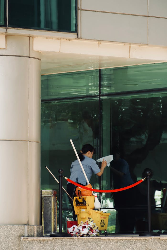 services-02 Person cleaning a glass window of a tall building with cleaning equipment visible.