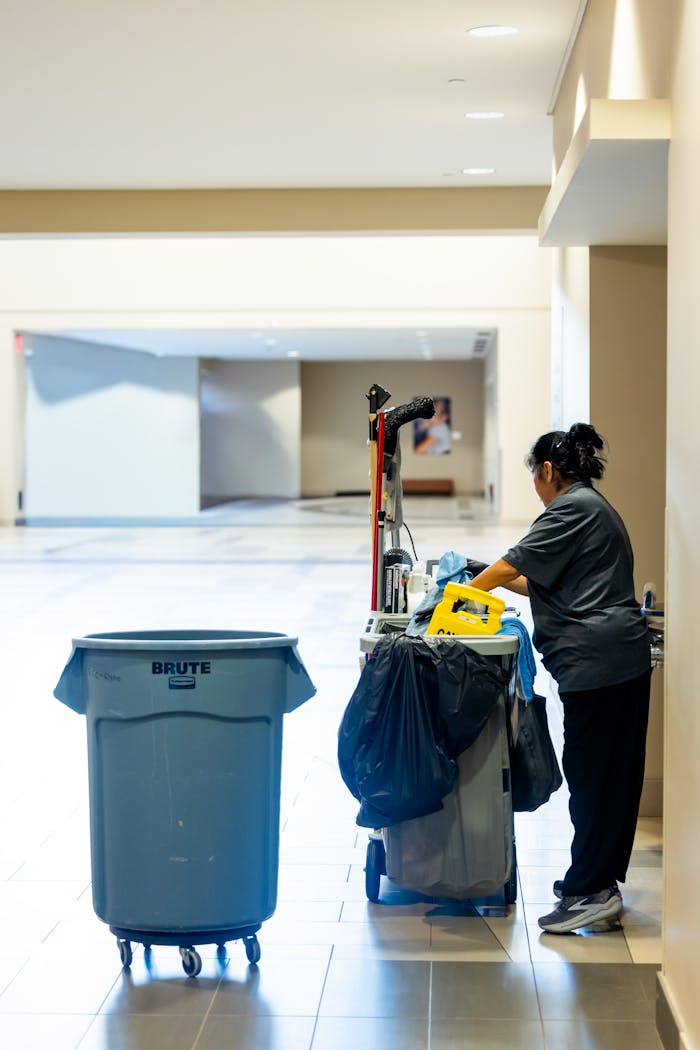 services-01 A janitorial worker pushes a cleaning cart in a spacious indoor hallway.